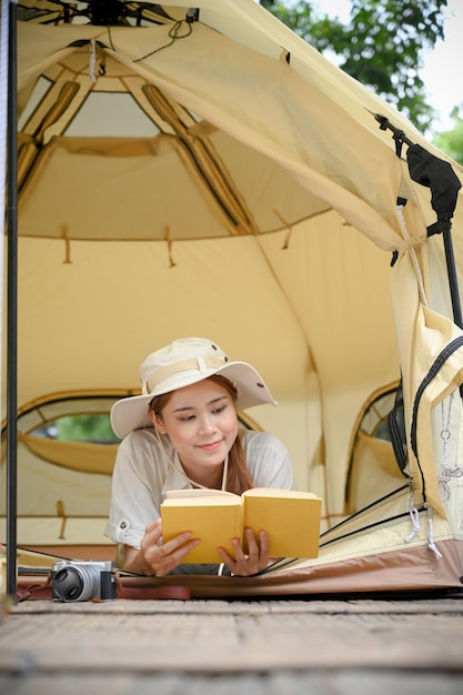 Belle jeune femme asiatique allongée dans la tente de camping et lisant un livre