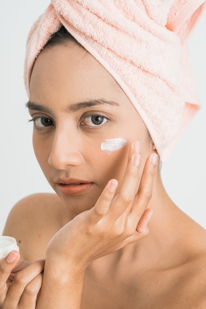 Belle jeune femme asiatique appliquant une crème cosmétique sur son visage