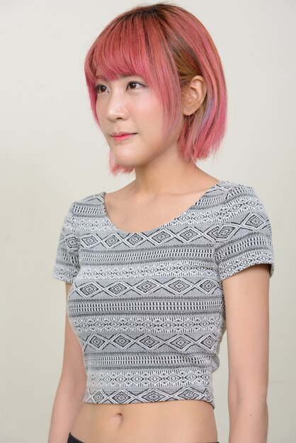 Belle jeune femme asiatique aux cheveux roses contre le mur blanc