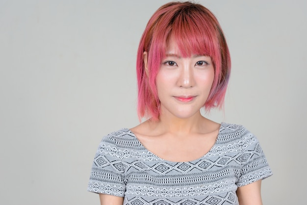 Belle jeune femme asiatique aux cheveux roses contre le mur blanc