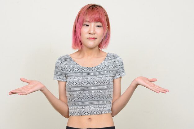 Belle jeune femme asiatique aux cheveux roses contre le mur blanc