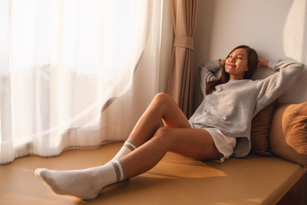 Photo une belle jeune femme asiatique aux yeux fermés assise et relaxante sur un canapé à la maison
