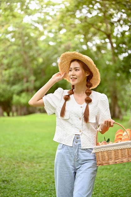 Une belle jeune femme asiatique avec un beau chapeau de paille marchant ou se promenant dans le parc verdoyant