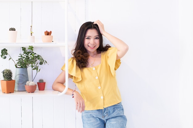 Belle jeune femme asiatique contre le mur en bois blanc et les étagères de cactus.