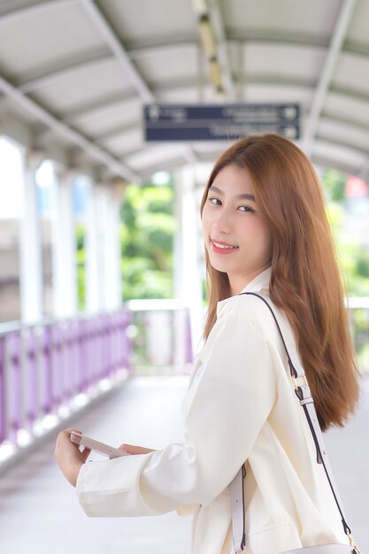 Belle jeune femme asiatique en costume blanc est sortie pour rencontrer un client au bureau de bonne humeur avec un fond de ville.