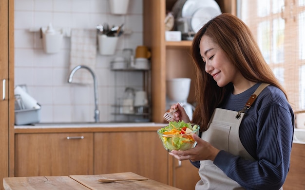 Une belle jeune femme asiatique cuisinant et mangeant une salade de légumes mélangés frais dans la cuisine à la maison