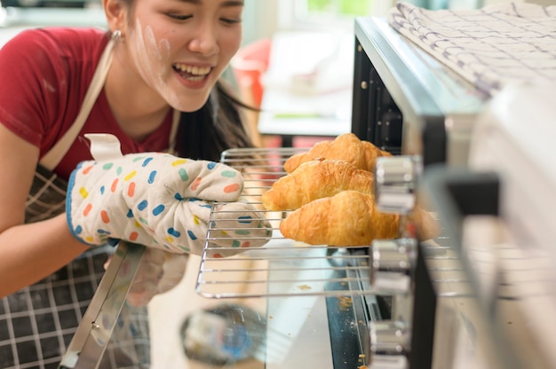 Une belle jeune femme asiatique cuit dans sa cuisine, sa boulangerie et son café