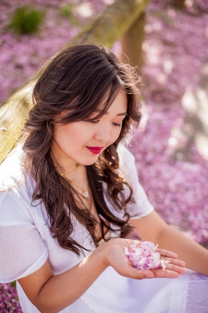 Une belle jeune femme asiatique dans une robe blanche se promène dans un parc fleuri. Sakura. Arbres en fleurs. Printemps.