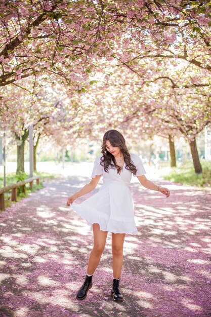 Une belle jeune femme asiatique dans une robe blanche se promène dans un parc fleuri. Sakura. Arbres en fleurs. Printemps.