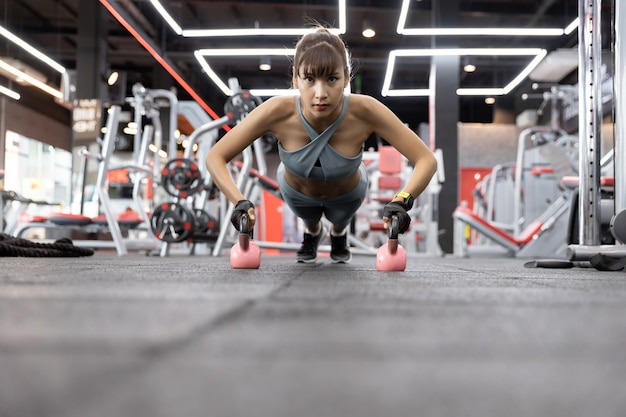 Belle jeune femme asiatique faire des exercices avec kettlebell. Push-up sur des poids à la gym.