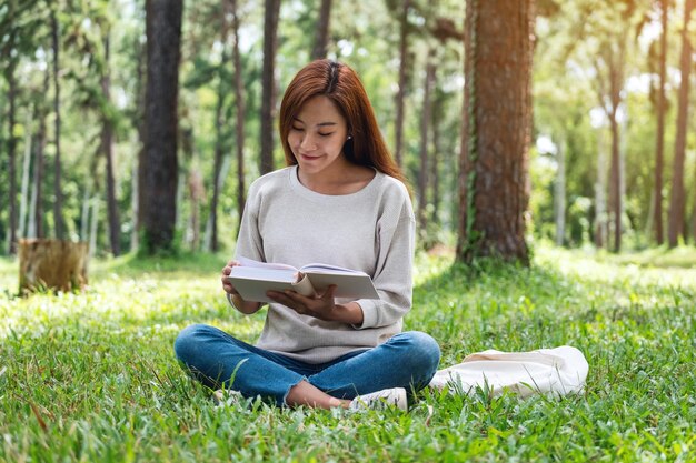 Une belle jeune femme asiatique lisant un livre assis dans le parc
