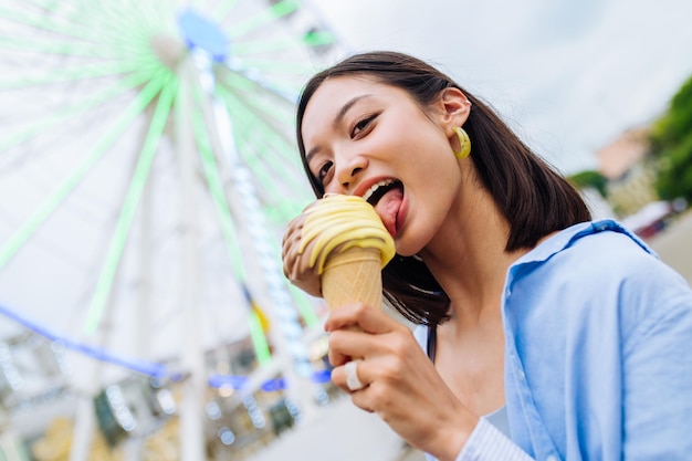 Belle jeune femme asiatique, manger des glaces au parc d'attractions