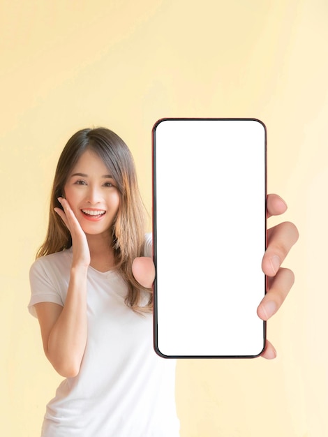 Belle jeune femme asiatique montrant un grand téléphone intelligent avec écran blanc écran blanc espace de copie vide pour bannière publicitaire isolé sur fond jaune Mock Up Image