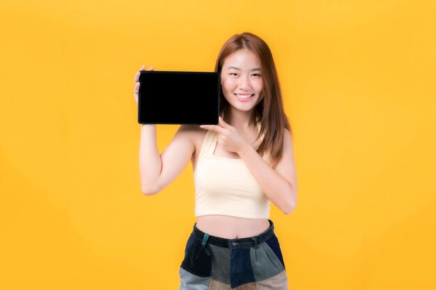 belle jeune femme asiatique montrant un téléphone intelligent tablette ordinateur avec écran vide écran noir espace de copie vide pour la publicité bannière isolée sur sur fond jaune Mock Up Image