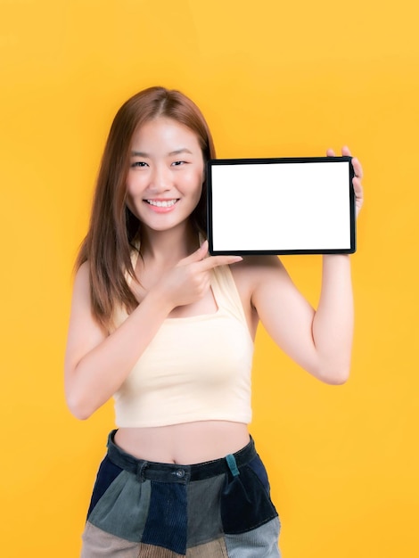 Belle jeune femme asiatique montrant un téléphone intelligent tablette téléphone ordinateur avec écran blanc écran blanc espace de copie vide pour bannière publicitaire isolé sur fond jaune Mock Up Image