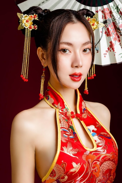 Belle jeune femme asiatique avec une peau fraîche et propre vêtue d'une robe traditionnelle cheongsam qipao tenant un ventilateur posant sur fond rouge Portrait de modèle féminin en studio Joyeux nouvel an chinois