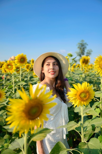 Belle jeune femme asiatique porte un chapeau debout et souriant dans un jardin fleuri de tournesol en journée ensoleillée