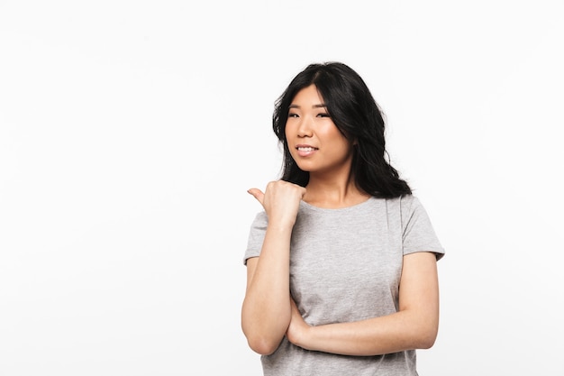 belle jeune femme asiatique posant isolé sur mur blanc pointant.