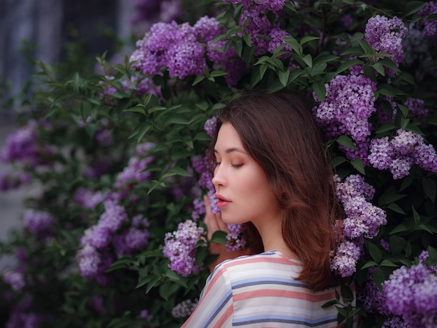 Belle jeune femme asiatique profitant de la floraison des fleurs lilas au printemps. Maquillage nu. Portrait en gros plan dans de beaux buissons de lilas violets