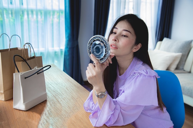 Belle jeune femme asiatique regardant miroir avec des sacs à provisions sur planche de bois.