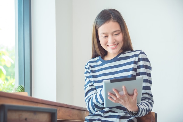 Belle jeune femme asiatique souriante tout en utilisant l&#39;ordinateur tablette à la maison