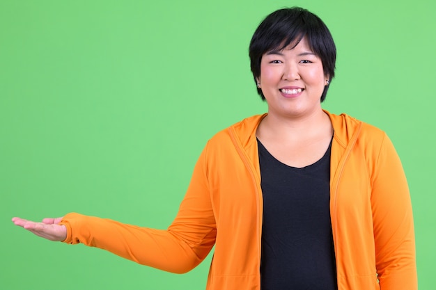 Belle jeune femme asiatique en surpoids prêt pour la salle de sport contre la clé de chrominance avec mur vert