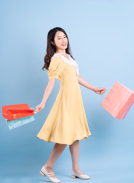 Belle jeune femme asiatique tenant un sac à provisions sur fond bleu