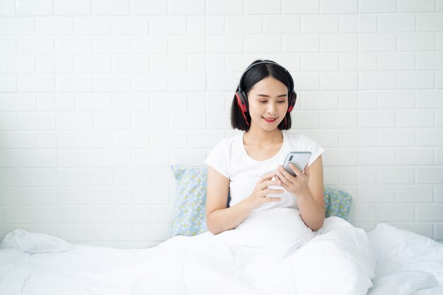 Belle jeune femme asiatique thaïlandaise avec casque ou écouteur se détendre sur le lit