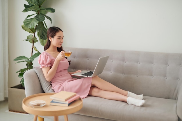 Belle jeune femme asiatique utilisant un ordinateur portable alors qu'elle était assise dans le salon et buvait du café