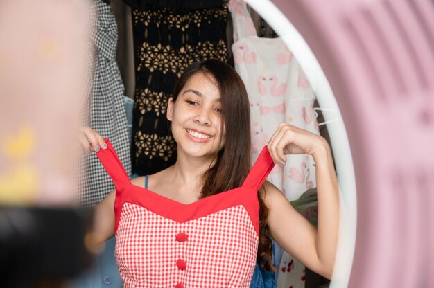 Belle jeune femme asiatique vendant des vêtements en ligne en streaming en direct par smartphone dans la maison