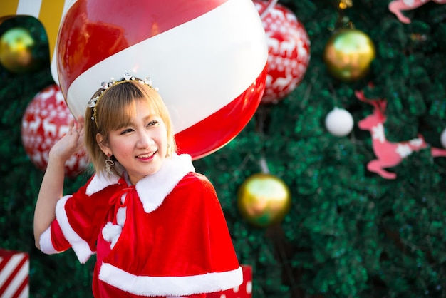 Belle jeune femme asiatique en vêtements de Père Noël à l'extérieurThaïlandaisEnvoyé du bonheur pour les enfantsJoyeux NoëlBienvenue en hiverFond de Noël décoré