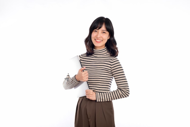 Belle jeune femme asiatique sur des vêtements pull tenant un ordinateur portable et regardant la caméra avec un visage souriant isolé sur fond blanc