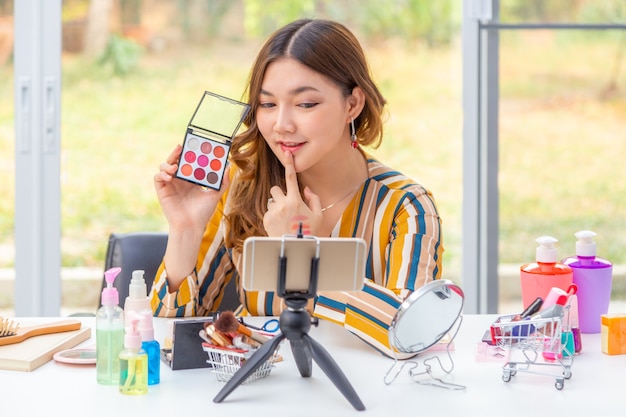 Belle jeune femme asiatique, vlogger, passant en revue les produits de beauté sur un blog vidéo via son téléphone à la maison