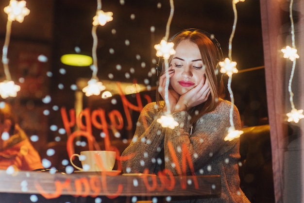 Belle jeune femme assise au café, buvant du café. Modèle écoutant de la musique.