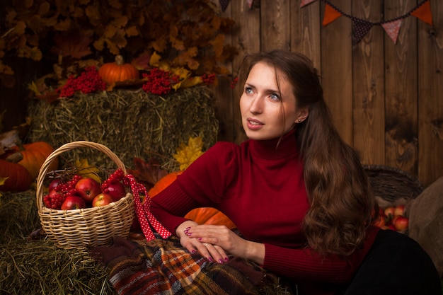 Belle jeune femme assise en automne sur le foin avec un panier de pommes et Rowan