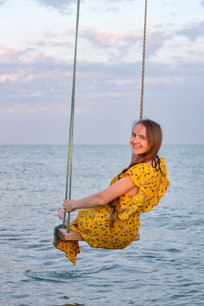 Belle jeune femme assise sur une balançoire corde sur fond de mer.