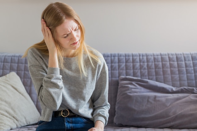 Belle jeune femme assise sur le canapé et ayant mal à la tête