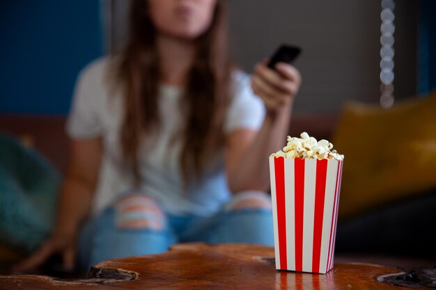 Belle jeune femme assise sur un canapé du salon, regardant la télévision avec une boîte en carton à rayures rouges et blanches avec pop-corn rétro boîte à pop-corn soirée cinéma