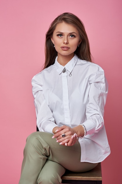 belle jeune femme assise sur une chaise sur fond rose