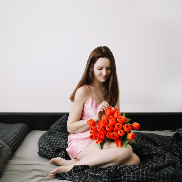 Belle jeune femme assise dans son lit et tenant un bouquet de tulipes rouges