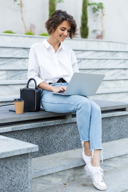 Belle jeune femme assise à l'extérieur à l'aide d'un ordinateur portable