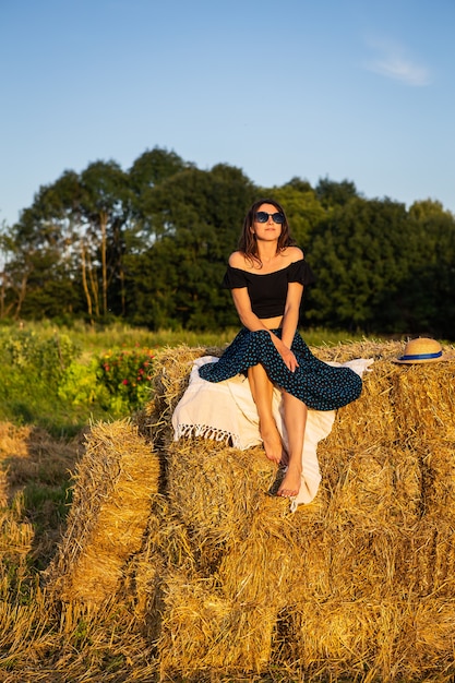 Belle jeune femme assise sur un gros tas de bottes de paille