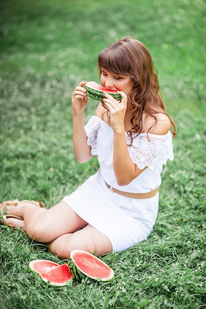 Belle jeune femme assise sur l'herbe et manger de la pastèque. Fille heureuse reposant sur l'herbe. Des étés chauds. Pastèque.