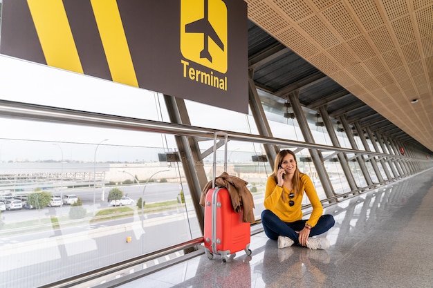 Belle jeune femme assise sur le sol en attente à l'aéroport avec ses bagages