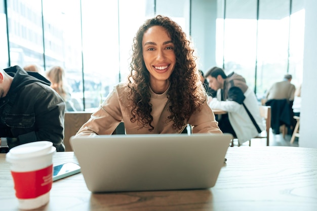 Une belle jeune femme assise à la table et utilisant un ordinateur portable dans un café