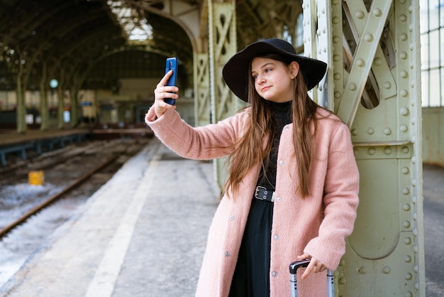 Belle jeune femme attendant le train à la gare pour voyager en automne avec le téléphone à la main il ...