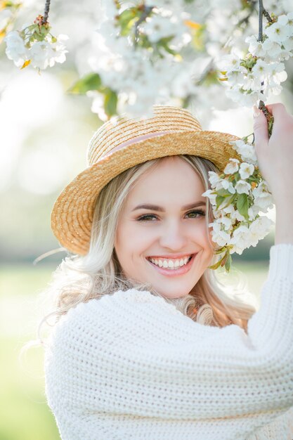 Belle jeune femme au chapeau en osier se repose sur un pique-nique dans un jardin fleuri. Fleurs blanches. Printemps. Joie.