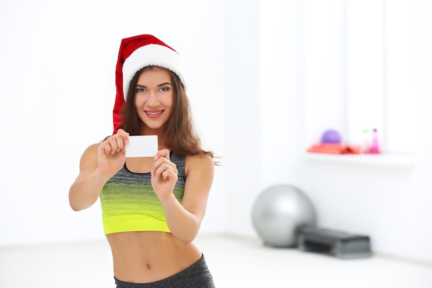 Belle jeune femme au chapeau de père Noël avec carte au gymnase