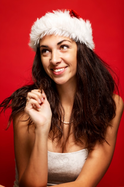 Belle jeune femme au chapeau de père Noël rit. Verticale. Rouge .