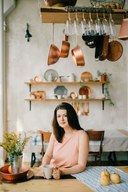 Belle jeune femme au foyer en robe prenant son petit déjeuner dans la cuisine